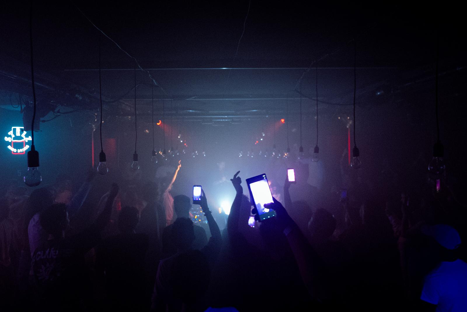 Crowd with raised phones in a dark, fog-filled club